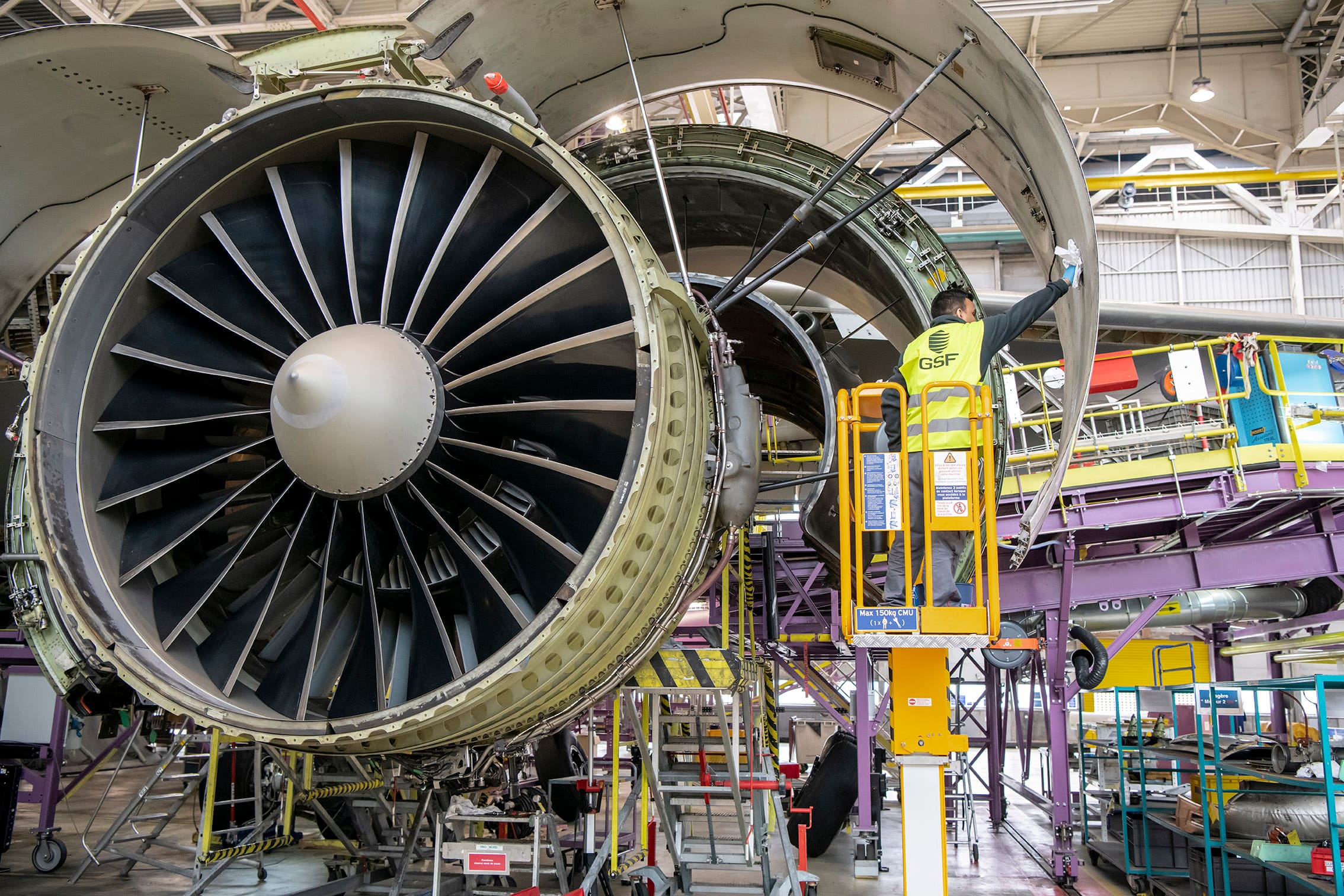 GSF team member on a lift, working beside an aircraft engine in a hangar.